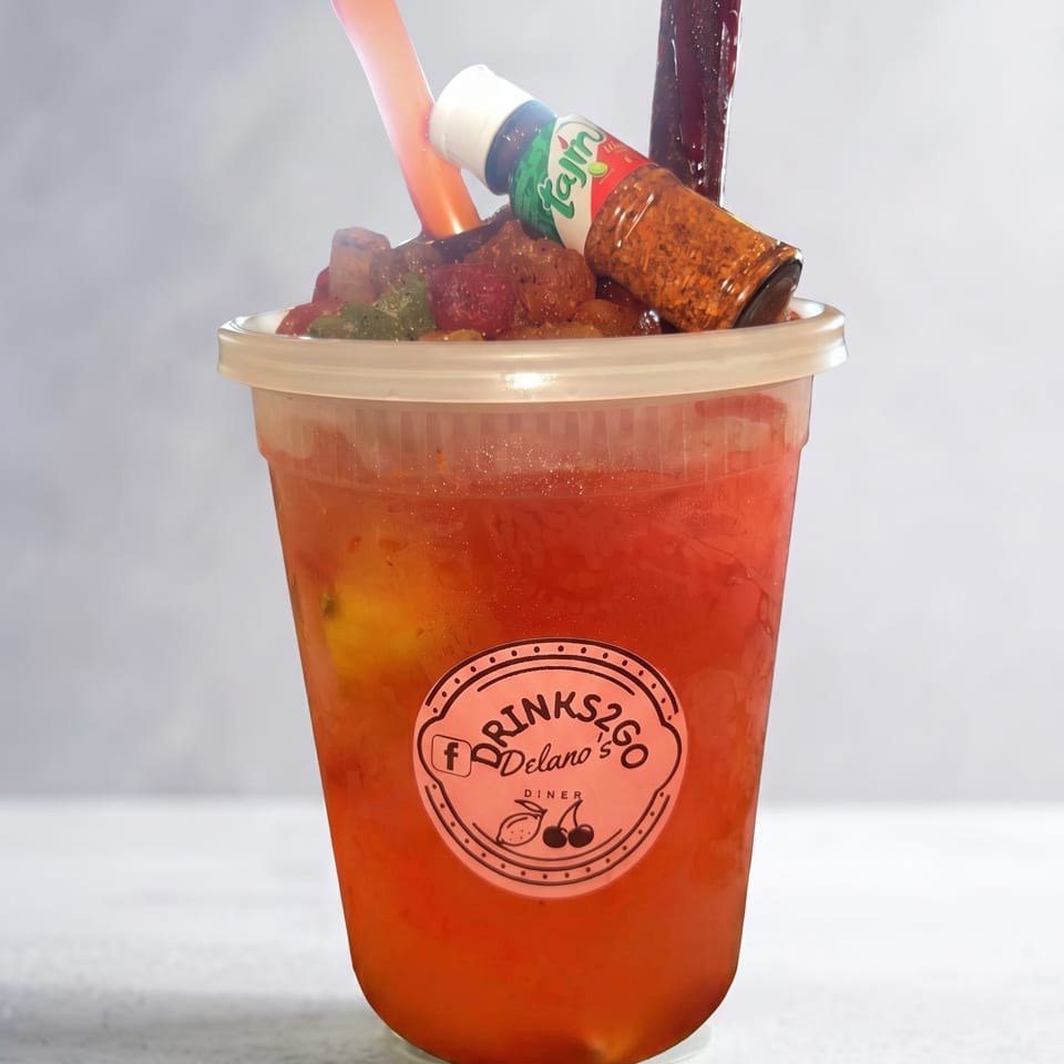 A red drink in a clear plastic cup with a Tajin bottle, candy, and a straw.