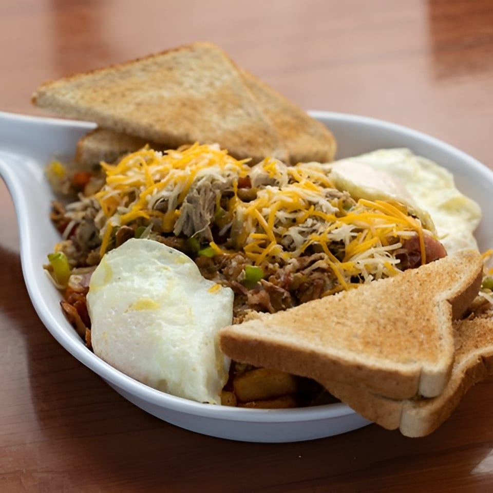 Breakfast skillet with shredded meat, cheese, eggs, and toast in a white dish on a wooden table.