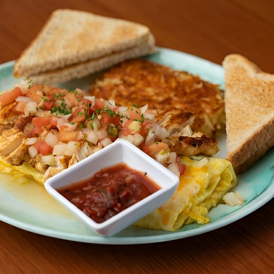 Breakfast plate with scrambled eggs, hash browns, chicken with pico de gallo, salsa, and toast.