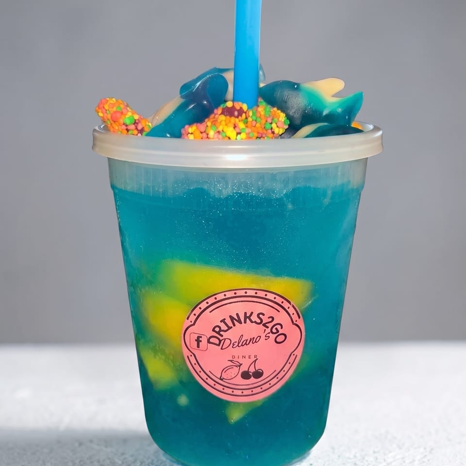 Blue slushie drink with gummy sharks, colorful sprinkles, and a blue straw in a clear cup.